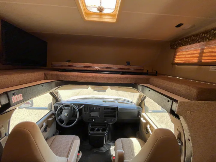 Spacious rv rental interior with front cockpit, dashboard, seats, and cozy cab-over bunk bed.. Coachmen Leprechaun 2019
