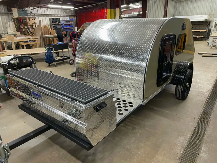 Newly built teardrop RV camper in a workshop, showcasing diamond plate exterior, front storage, and solar panel. Perfect for **RV rental**.. TC Tear Drop TC Original 2022