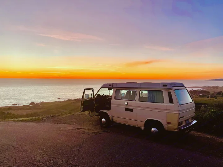 Camper van parked at sunset by the ocean. Ideal RV rental for coastal adventures & van life.. Volkswagen Vanagon 1984