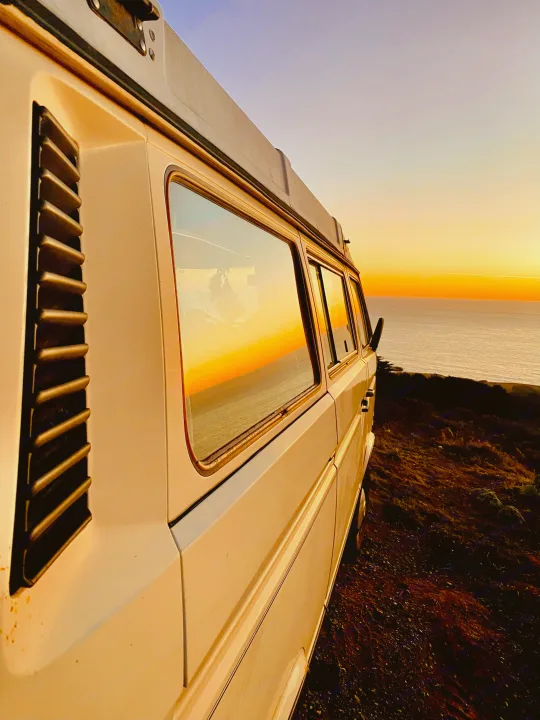 A white RV rental enjoys a stunning sunset view by the ocean. Perfect for coastal van life adventures.. Volkswagen Vanagon 1984