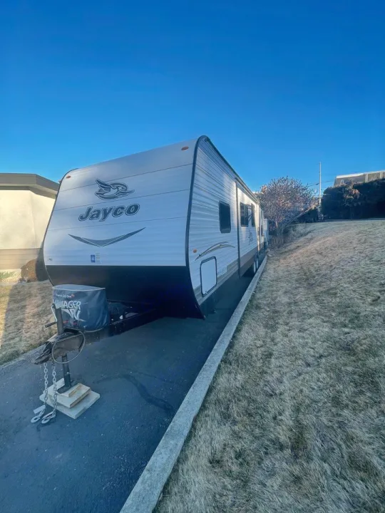 A white and black Jayco travel trailer is parked on asphalt under a clear blue sky, perfect for an rv rental adventure.. Jayco 32 BHS 2017