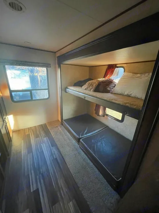 Inside an RV rental bunkhouse: a bright top bunk with bedding, two floor mattresses, and a window for views. Ready for your next adventure.. Jayco 32 BHS 2017