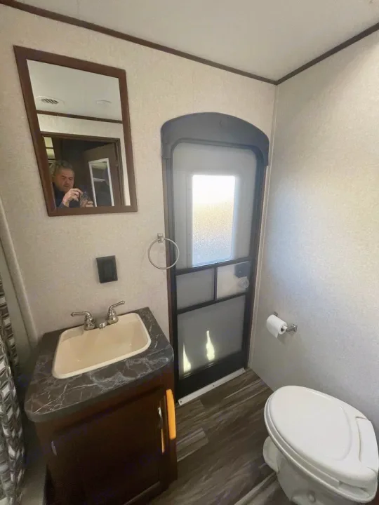 RV rental interior: compact bathroom with sink, toilet, and door. Mirror reflects photographer.. Jayco 32 BHS 2017