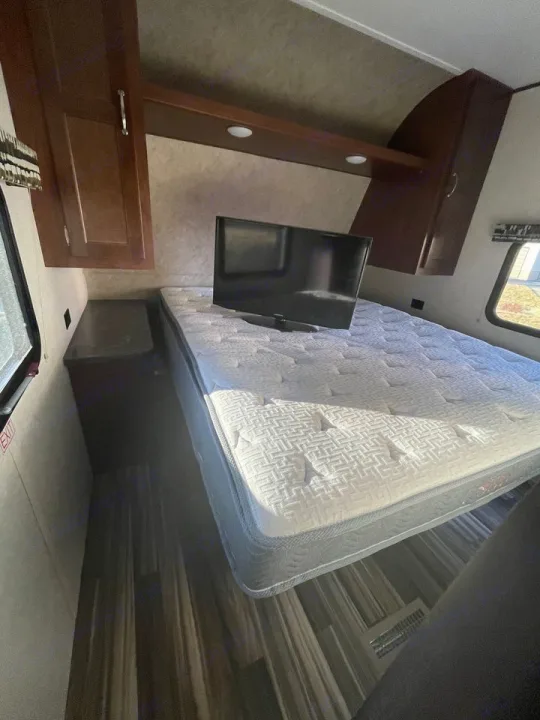 RV rental bedroom interior: Features a large mattress with a TV, dark wood cabinets, and side windows.. Jayco 32 BHS 2017