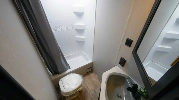 Compact RV rental bathroom: covered toilet, shower with grey curtain, and sink vanity. Ready for your travel trailer adventures.. Forest River Cherokee Grey Wolf Special Edition 2021