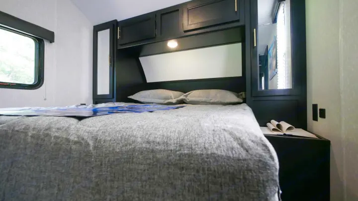 Cozy RV rental bedroom with a grey bed, built-in black cabinetry, and a window overlooking nature.. Forest River Cherokee Grey Wolf Special Edition 2021