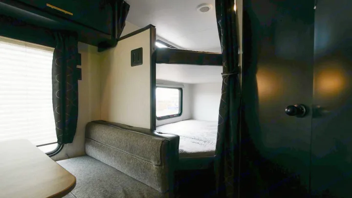 Interior of an RV rental featuring a cozy dining area with a table and bench seats on the left, next to built-in bunk beds.. Forest River Cherokee Grey Wolf Special Edition 2021
