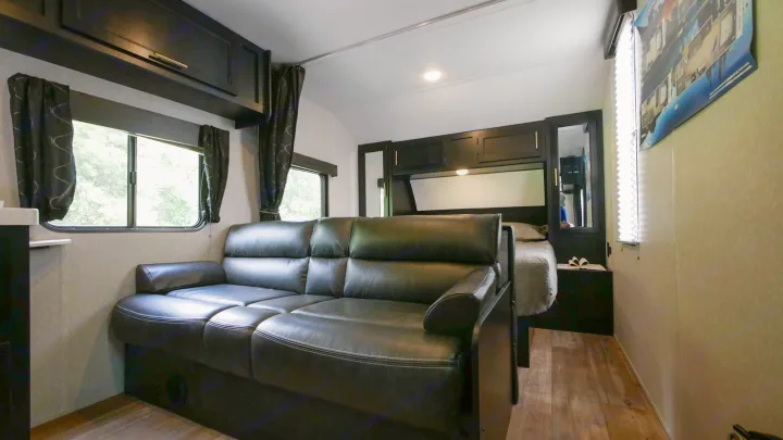 RV rental: View inside a modern RV showing a black leather sofa in the living area, leading to a compact bedroom.. Forest River Cherokee Grey Wolf Special Edition 2021