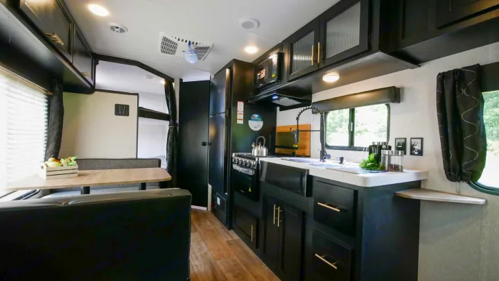 Modern RV rental interior with black kitchen cabinets, a dining area, and bunk beds visible in the background.. Forest River Cherokee Grey Wolf Special Edition 2021