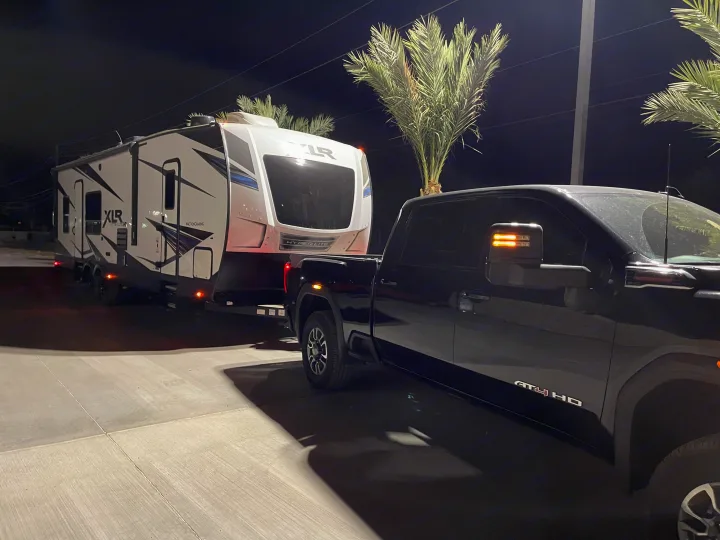A black AT4 HD truck is hooked to a white XLR Hyper Lite fifth-wheel RV at night. Ready for an RV rental trip!. Forest River Xlr Thunrderbolt 2021