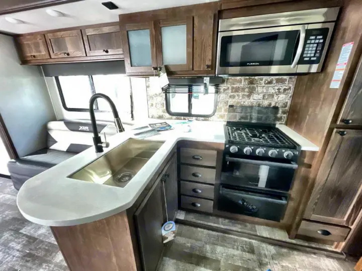 Fully equipped RV rental kitchen featuring a stainless steel sink, microwave, and stove, with wood cabinetry.. Forest River Xlr Thunrderbolt 2021