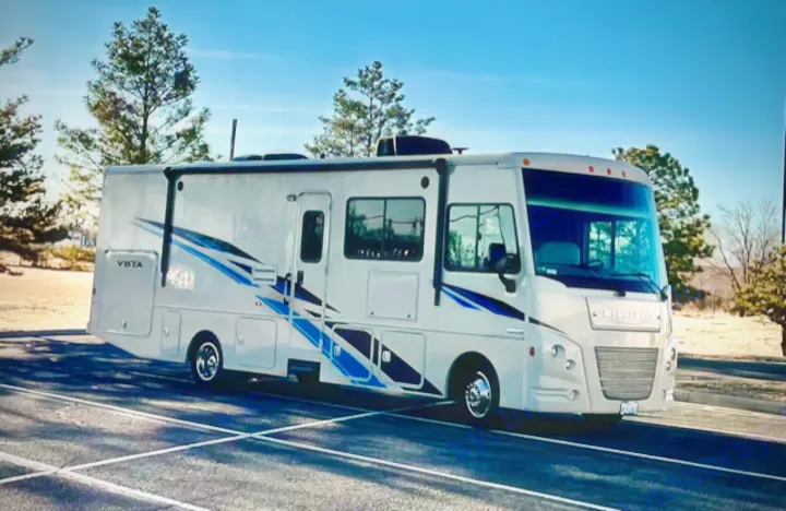 Spacious light gray Winnebago Vista RV rental motorhome with blue stripes, parked for your next journey.. Winnebago Vista 2019