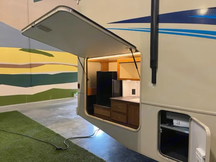 This RV rental features an outdoor kitchen with a fridge, counter, and cabinets, plus an open storage compartment.. Winnebago Vista 2019
