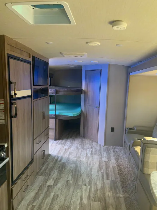 Inside a modern **RV rental**: kitchenette, bunk beds with bright mattresses, and a cozy lounge area.. Grand Design 2800BH 2021
