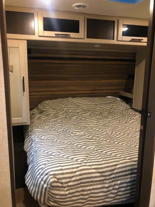 RV rental bedroom: cozy bed with striped comforter, overhead cabinets, and compact built-in storage.. Crossroads Cruiser Aire 2021