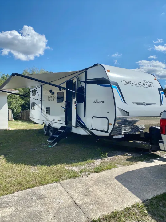 Bright blue sky over a parked Coachmen Freedom Express travel trailer with awning extended, perfect for an RV rental getaway.. Coachmen Freedom express select 2022