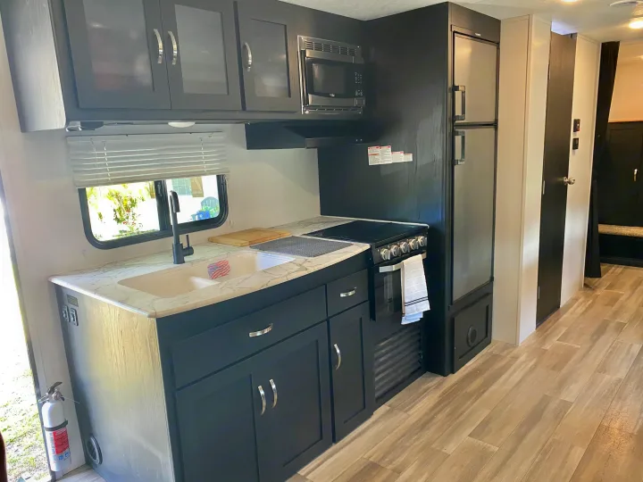 This RV rental features a modern kitchen with dark cabinetry, a spacious counter, sink, microwave, stove, and fridge.. Coachmen Freedom express select 2022
