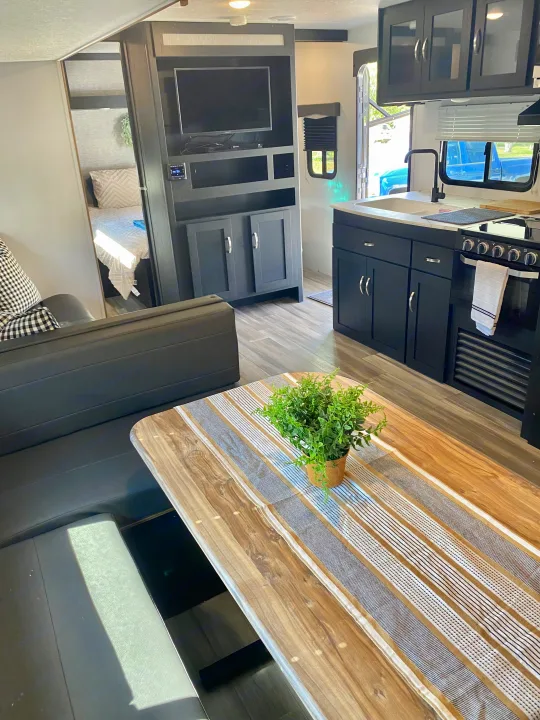 Modern RV rental interior with a black kitchen, wood dining table, and a clear view into the bedroom. A well-equipped travel space.. Coachmen Freedom express select 2022