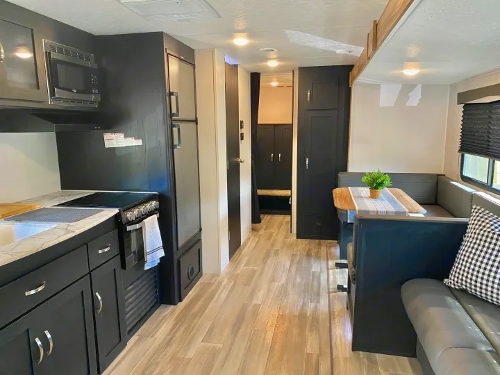 Modern RV rental interior with black kitchen cabinets, a full refrigerator, and a cozy U-shaped dinette perfect for meals.. Coachmen Freedom express select 2022