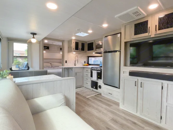 Spacious RV rental interior with modern kitchen, comfortable sofa, dining table, and a peek into the cozy bedroom.. East to West Alta 2022