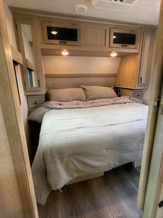 Explore this cozy RV rental bedroom. Features a comfy bed, built-in storage, and soft ambient lighting for your travel comfort.. East to West Alta 2022
