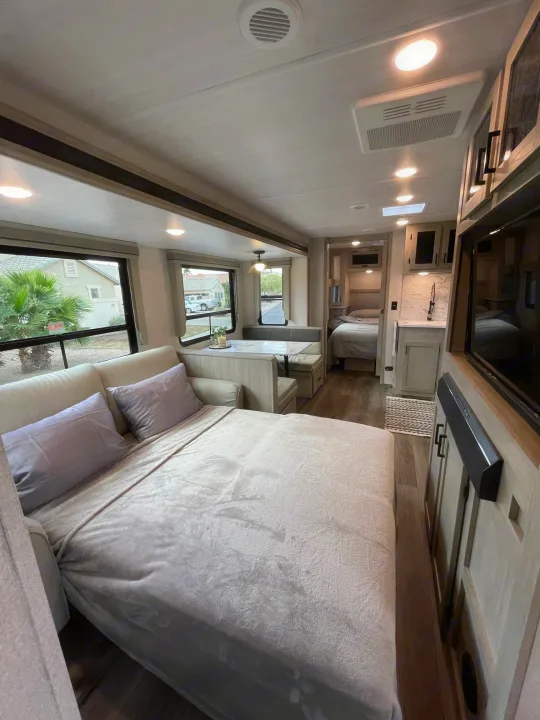 Inside a stylish RV rental: a cozy bed, living area with large windows, and full kitchen.. East to West Alta 2022