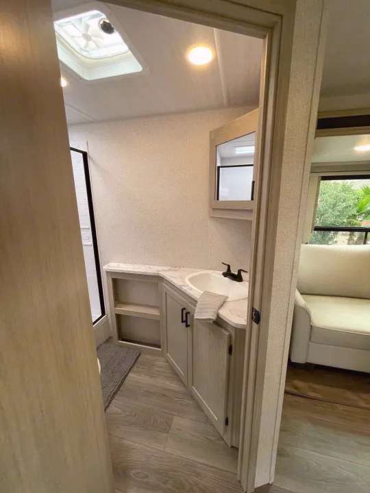 Spacious RV rental bathroom with modern sink, mirror, and bright interior. View into living area with window.. East to West Alta 2022