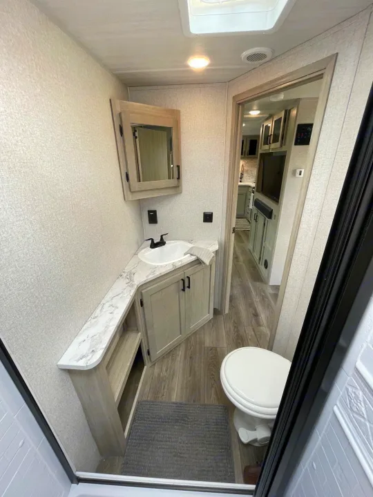 Modern rv rental interior featuring a bright bedroom area, marble vanity with sink, and adjacent toilet.. East to West Alta 2022