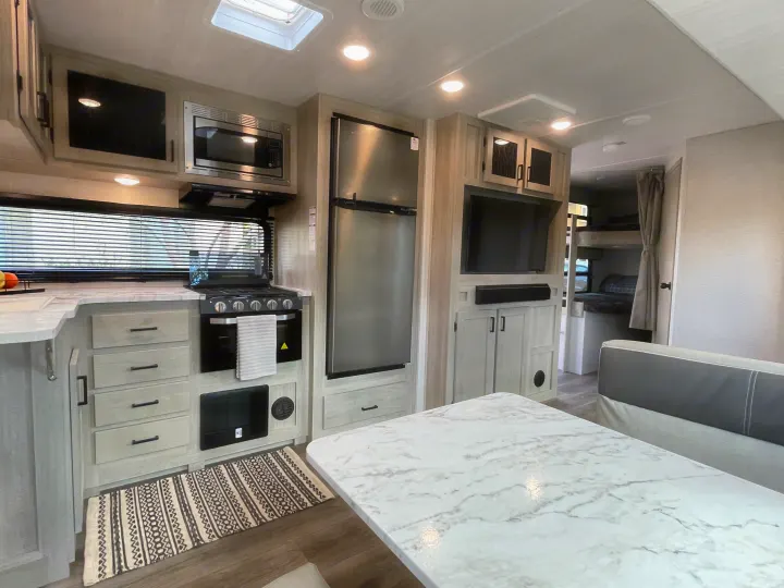 RV rental with full kitchen: microwave, stove, fridge, marble table, and living area extending to bunk beds.. East to West Alta 2022