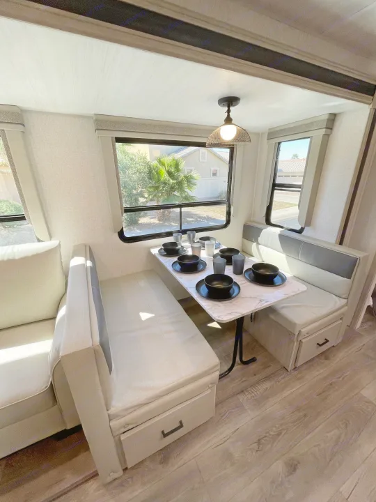 Spacious RV rental dinette featuring a modern table setting and comfortable bench seating by bright windows.. East to West Alta 2022