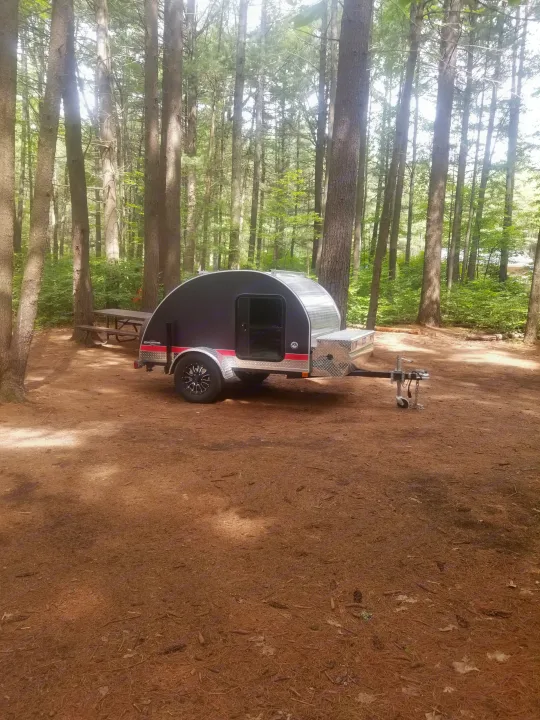 A black and silver teardrop rv rental trailer at a shady, pine-filled campground site, ready for adventure.. The Teardrop Trailer Diamond in the rough 2021