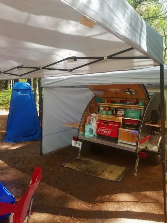 Compact RV rental setup: teardrop trailer with galley kitchen, privacy tent, and canopy at a sunny campsite.. The Teardrop Trailer Diamond in the rough 2021