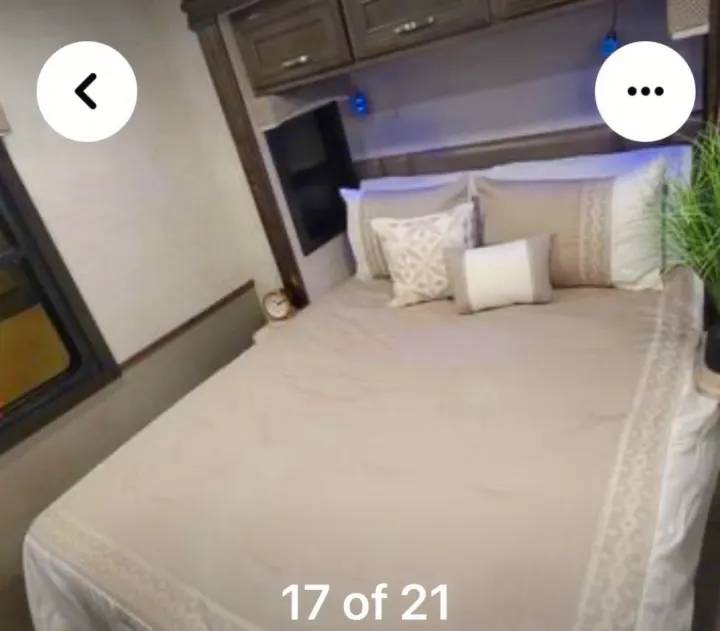 This inviting RV rental bedroom features a comfy bed with neutral linens, overhead cabinets, and a mounted TV for your travels.. Ford Motorhome Chassis 2020
