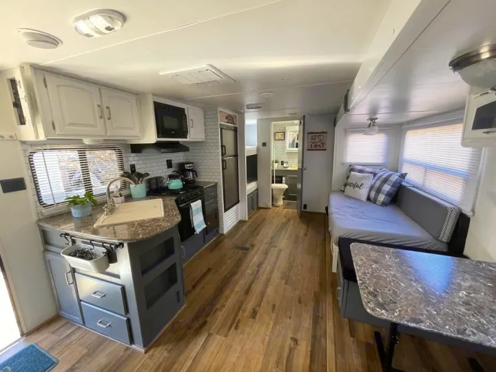 Cozy RV rental interior with a compact kitchen, gray counters, a daybed, and dining table on wood floors.. Keystone RV Springdale 2015