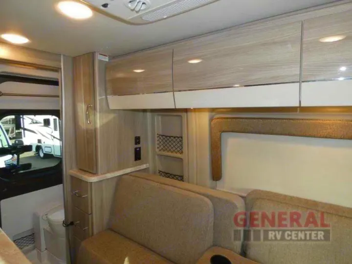 Bright RV rental interior showing light woodgrain cabinets, comfortable seating, and a compact bathroom.. Thor Scope 2022