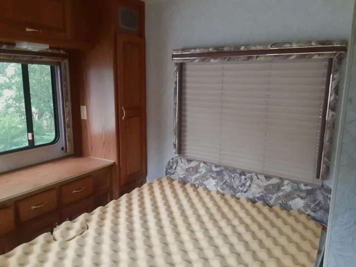 Cozy RV rental bedroom featuring wood cabinets, a window with outdoor views, and a bed with a foam topper & patterned headboard.. Jayco Eagle 1996