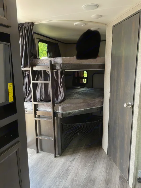 RV rental interior showing stacked bunk beds with privacy curtains, ladder, and a storage net below.. Jayco Jay Feather 2021