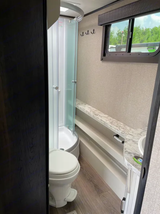 RV rental bathroom showing a corner shower, toilet, sink, and window. Clean and functional interior.. Jayco Jay Feather 2021