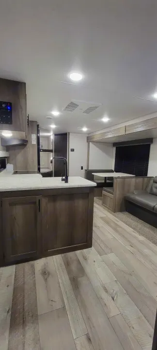 Spacious RV rental interior with a light wood kitchen island, dining booth, sofa, and bunks. Modern design.. Sportsmen SE 2021