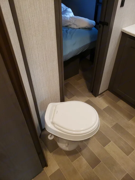 An RV rental interior features a compact Dometic toilet, with a peek into the cozy bedroom through an open doorway.. Cruiser RV MPG Ultra Lite 2020