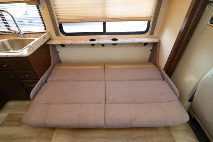 RV rental interior with a versatile convertible sofa-bed, kitchen sink, and overhead shelf with cup holders by the window.. Thor Freedom Elite 2019