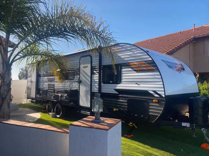This RV rental, a Wildwood X-Lite travel trailer, is parked in a sunny residential backyard with a palm tree.. Forest River 263BHXL 2022