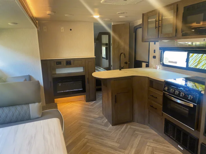 Spacious rv rental interior showing kitchen with stove, sink, and cabinets, a cozy living area with fireplace, and modern flooring.. Forest River 263BHXL 2022