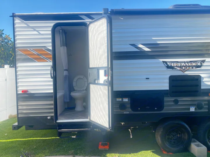 Get a peek inside this Forest River Wildwood RV rental! Bathroom with toilet & shower setup shown. Camper on grass.. Forest River 263BHXL 2022