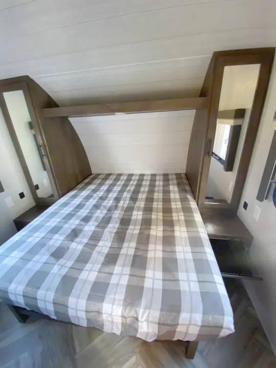RV rental bedroom: cozy queen bed with grey & white plaid comforter, mirrored storage on both sides.. Forest River 263BHXL 2022