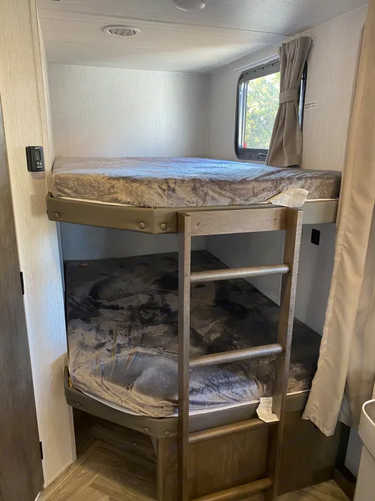 Explore an RV rental's bunk beds: two cozy bunks with fuzzy blankets, ladder, and window. Max 300 lbs capacity for comfortable travel.. Forest River 263BHXL 2022