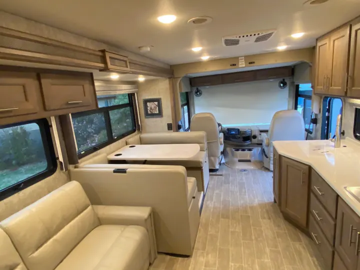 Bright RV rental interior featuring a beige dinette, sofa, kitchen, and driver's area for comfortable travel.. Thor 37.1 2022