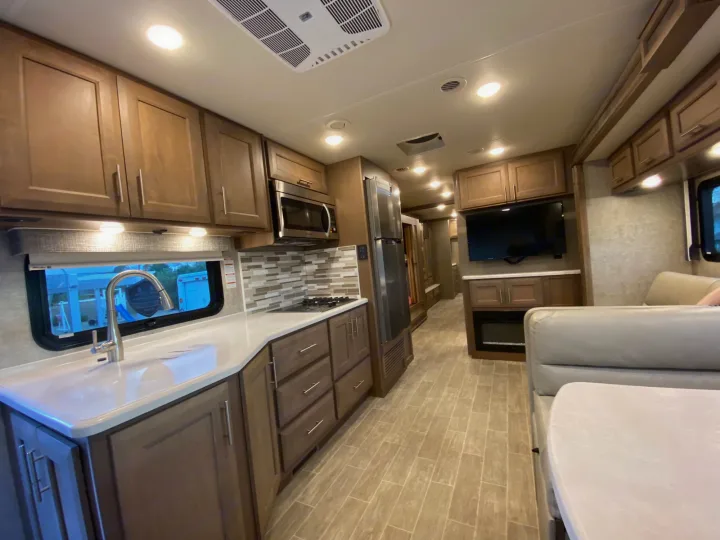 Inside a clean rv rental: full kitchen with light cabinets & counters, living area with TV, fireplace, and dining booth.. Thor 37.1 2022