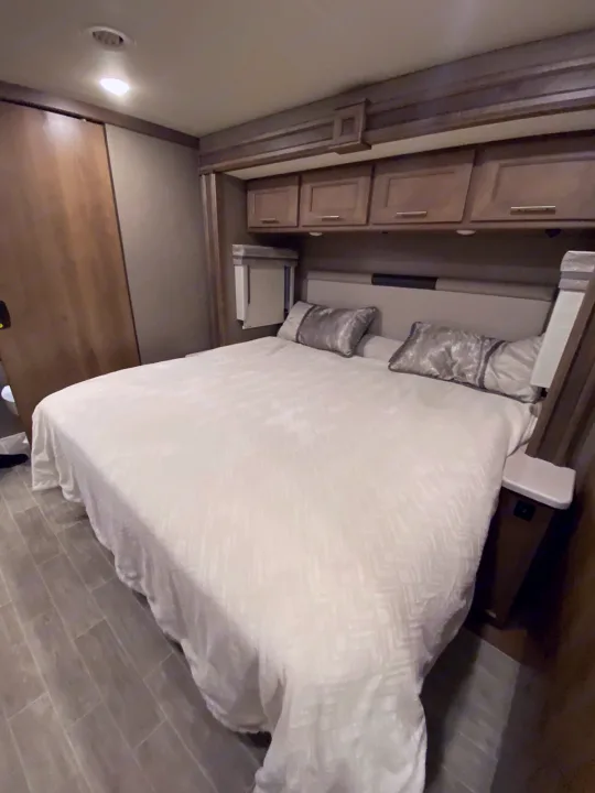 This RV rental features a cozy, compact bedroom with overhead storage, a comfortable bed, and wood-look flooring.. Thor 37.1 2022