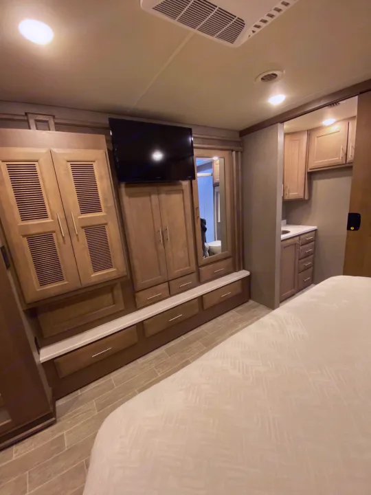 This RV rental bedroom features a comfy bed, built-in storage cabinets, a TV, and a compact bathroom vanity.. Thor 37.1 2022